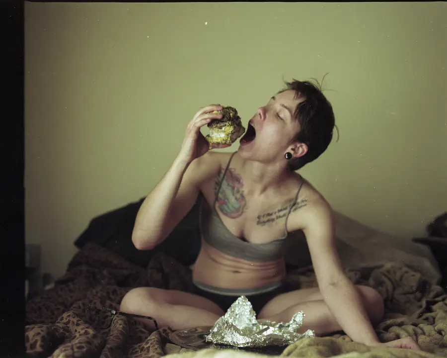 The girl opens her mouth wide and brings the rotten food to her mouth as if to eat it.