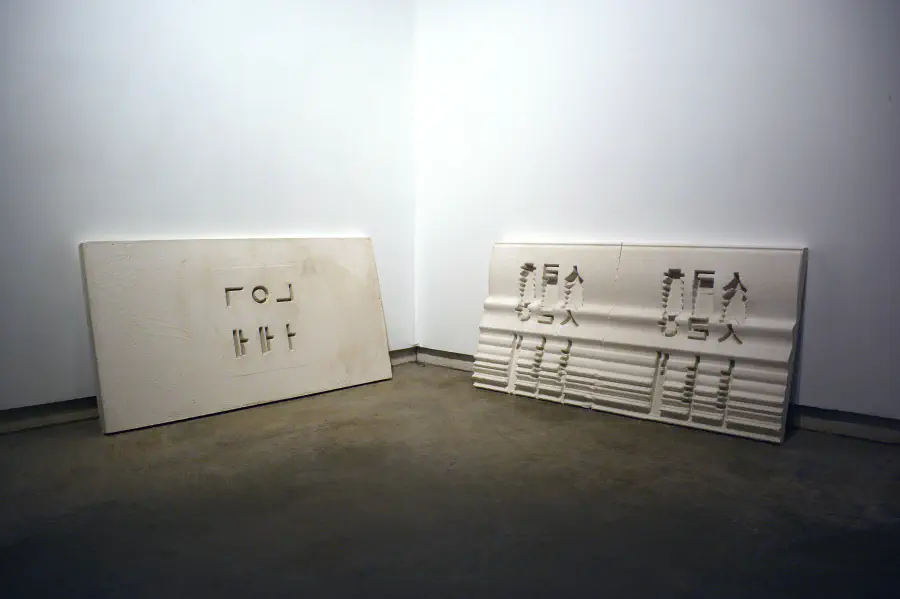 Wooden plank with Hangul characters and shapes laser burned out. By the side of the board are various lasered boards stacked atop one another.