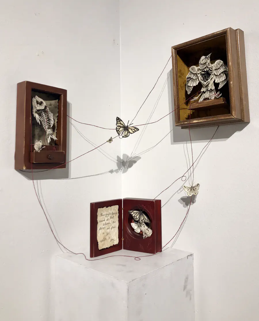 Three staggered box structures at different elevations. The top has a cut paper owl, the middle has a fish skeleton, and the bottom has butterflies. Strings connect each and have butterflies on them.