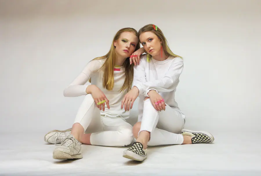 Two people dressed in white leaning against one another in an all white room.