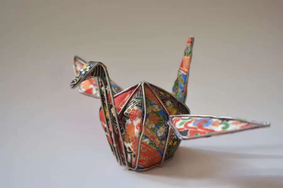 An origami paper crine with wire framing. The origami paper is red and blue. The wiring is delicate and gray.