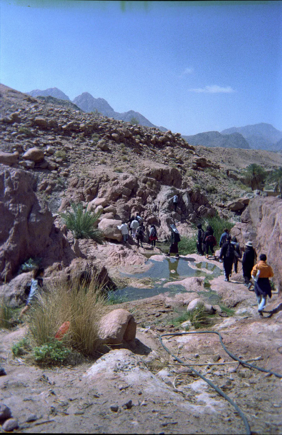 A photo of a pool in the mountains. A group of people walk past.